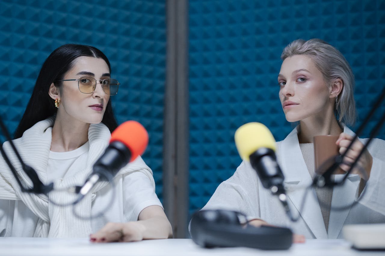 Two women in a soundproof studio with microphones, recording a podcast.